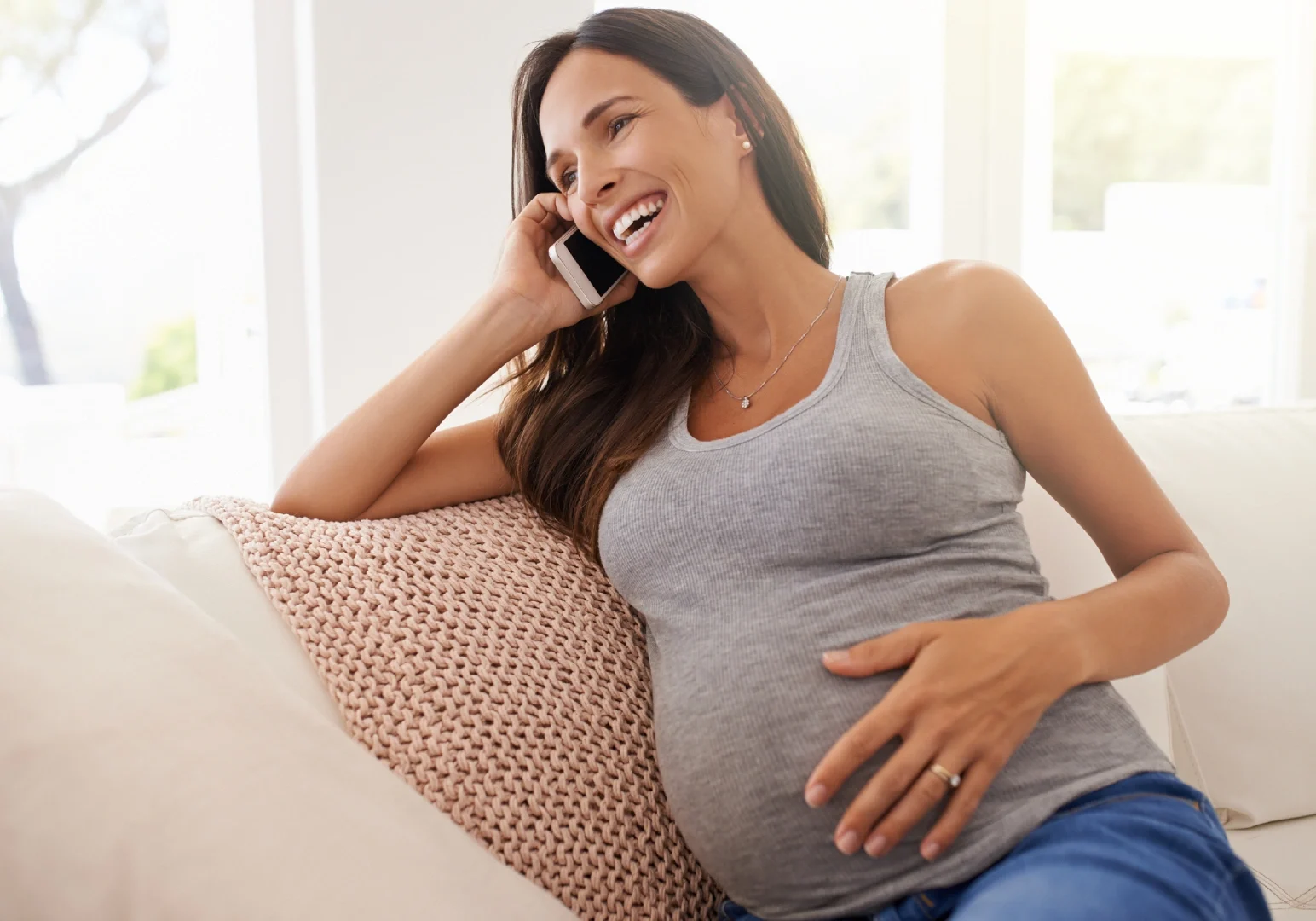 A pregnant woman sitting on the couch talking on her phone.